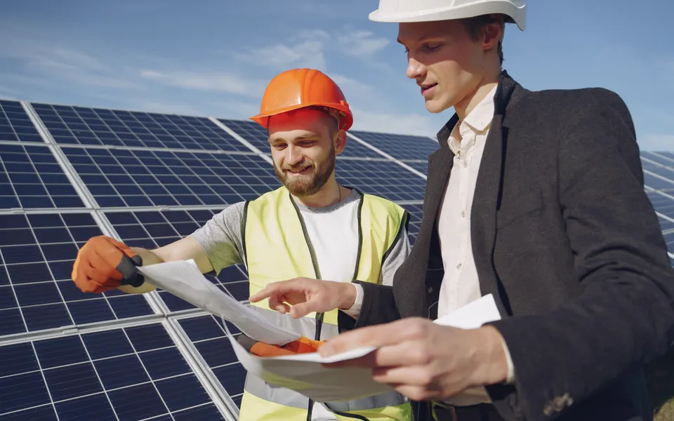 Two professionals discussing working drawings next to solar panels